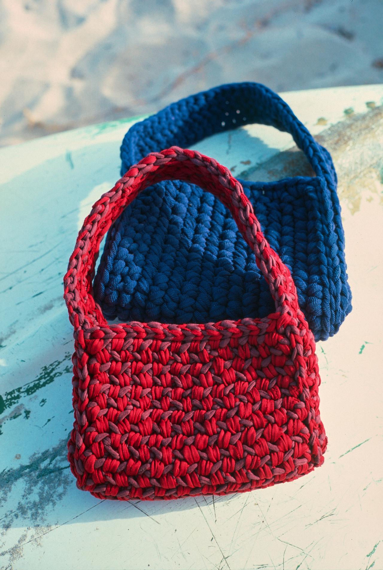 Bolso de ganchillo rojo delante de uno azul marino, sobre el casco desconchado de una barca