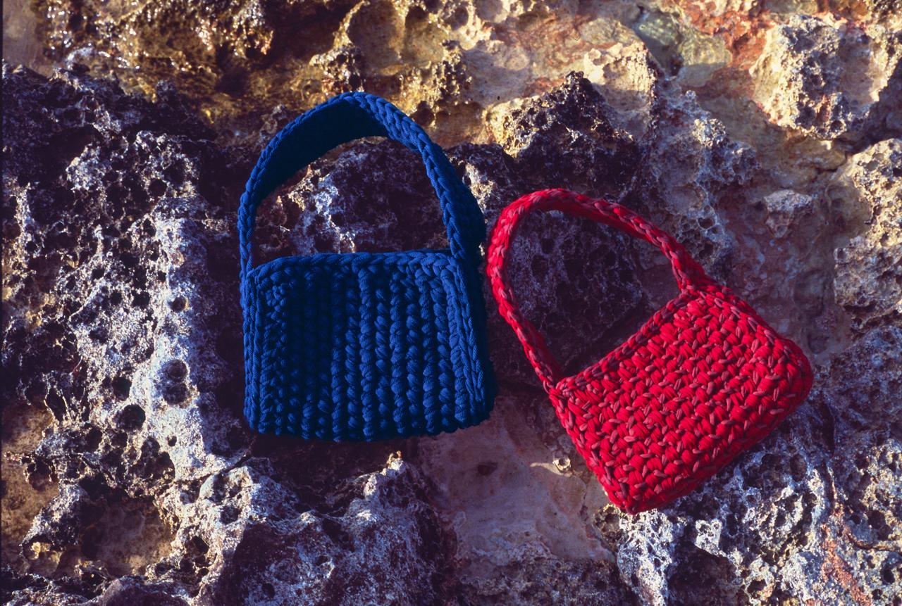 Bolsos de ganchillo azul marino y rojo, uno junto al otro sobre roca porosa de la costa