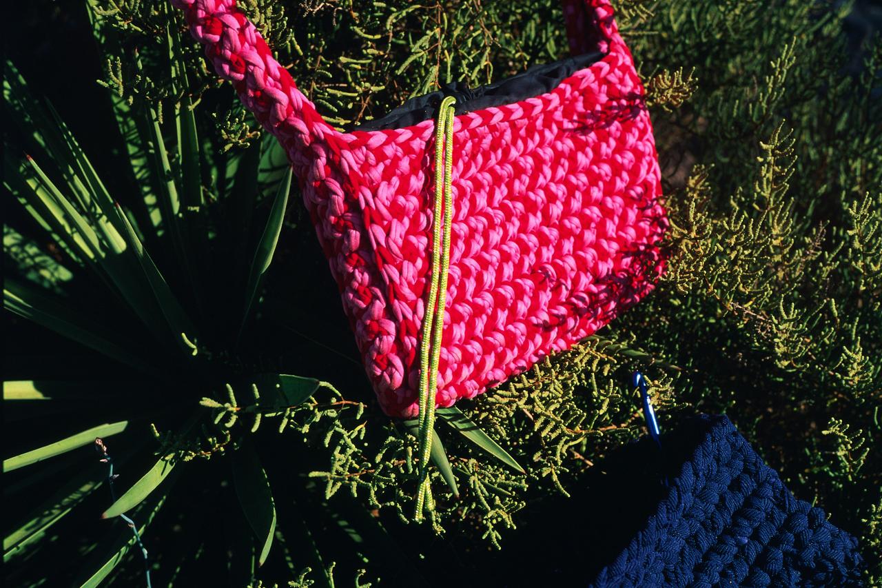Detalle de un bolso de ganchillo fucsia con cordón verde lima, junto a otro azul marino