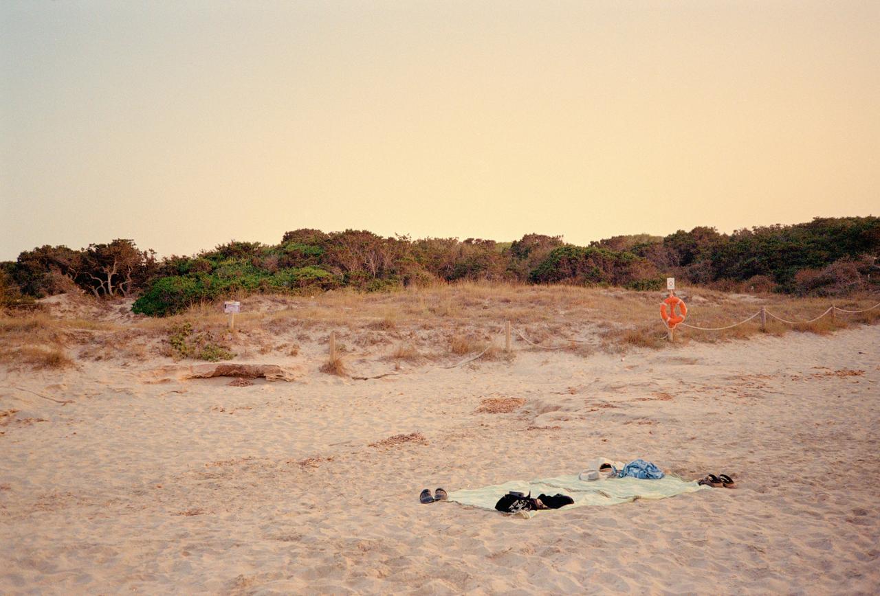 Toalla y ropa sobre la arena de una playa vacía al atardecer, junto a las dunas