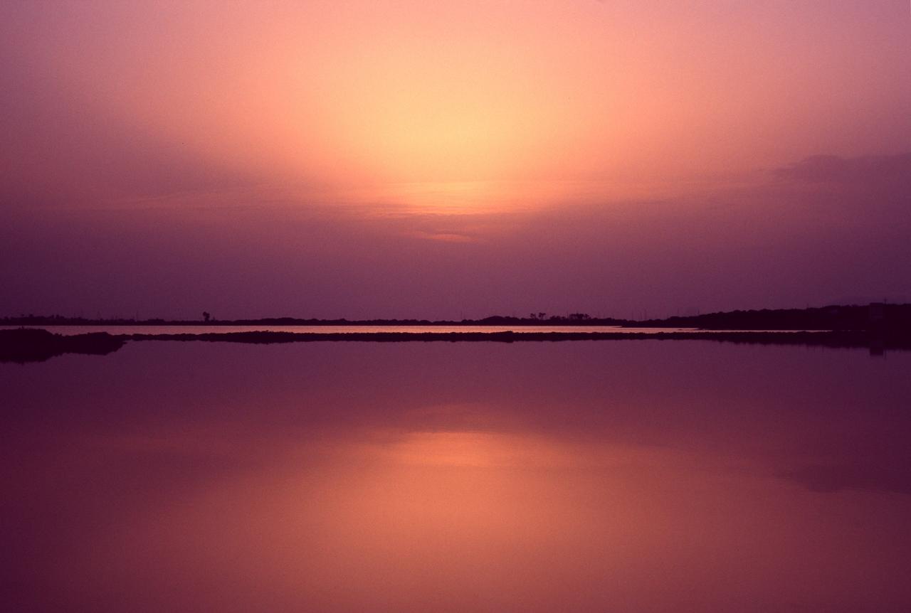 Laguna en calma que refleja un cielo rosado y violeta al atardecer