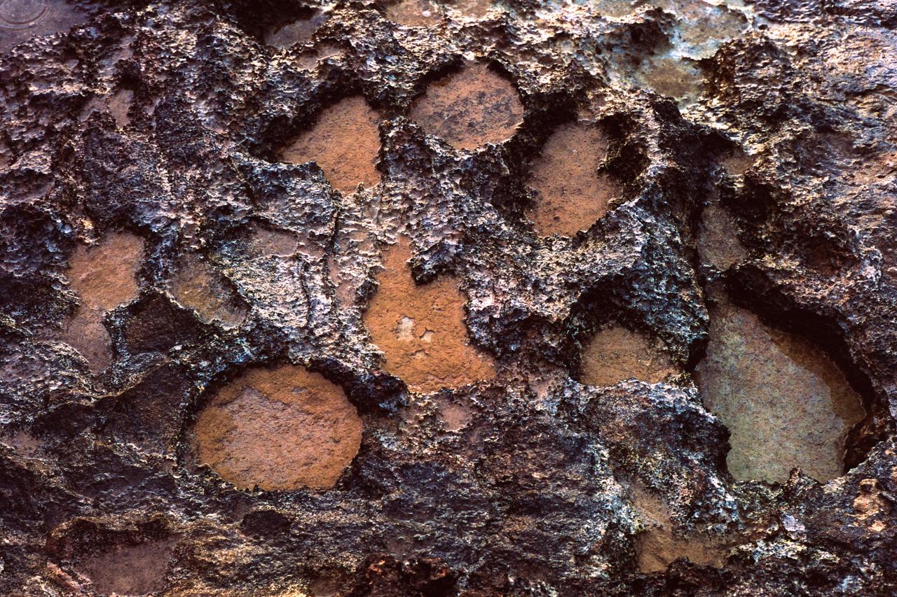 Textura de roca oscura con huecos redondeados rellenos de arena rojiza