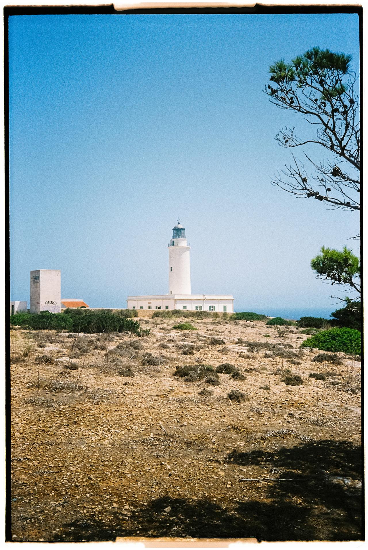 Faro blanco sobre una llanura pedregosa con matorral, bajo un cielo azul
