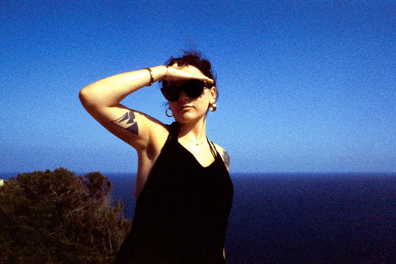 Mujer con gafas de sol haciéndose sombra con la mano, con el mar azul de fondo