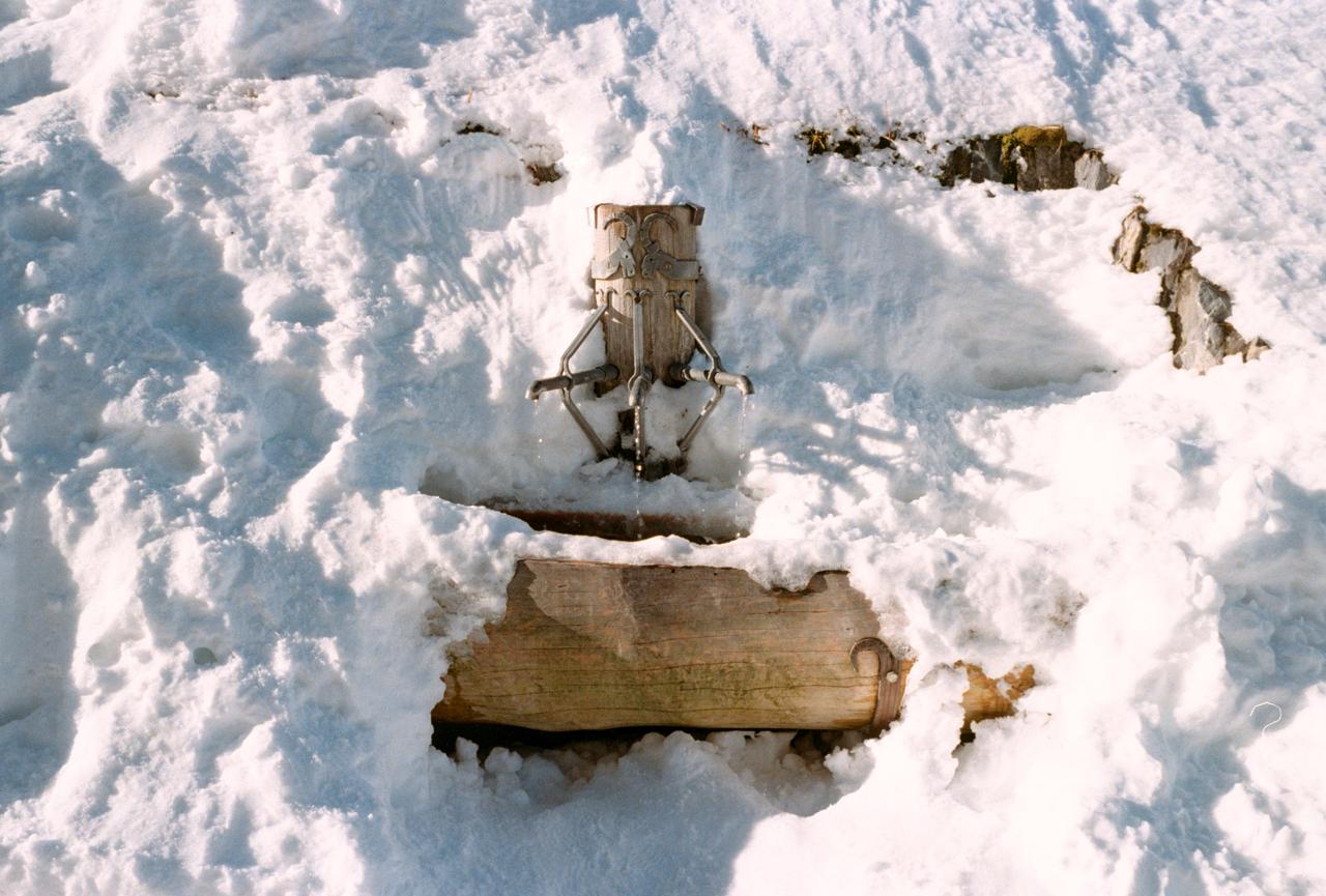 Pilón de madera de una fuente casi enterrado en la nieve