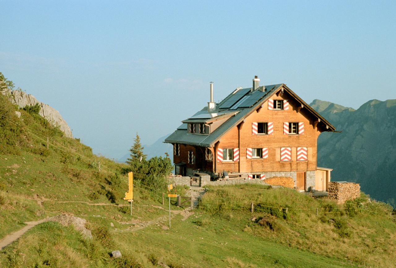 Refugio de montaña de madera con contraventanas rojas y blancas al atardecer