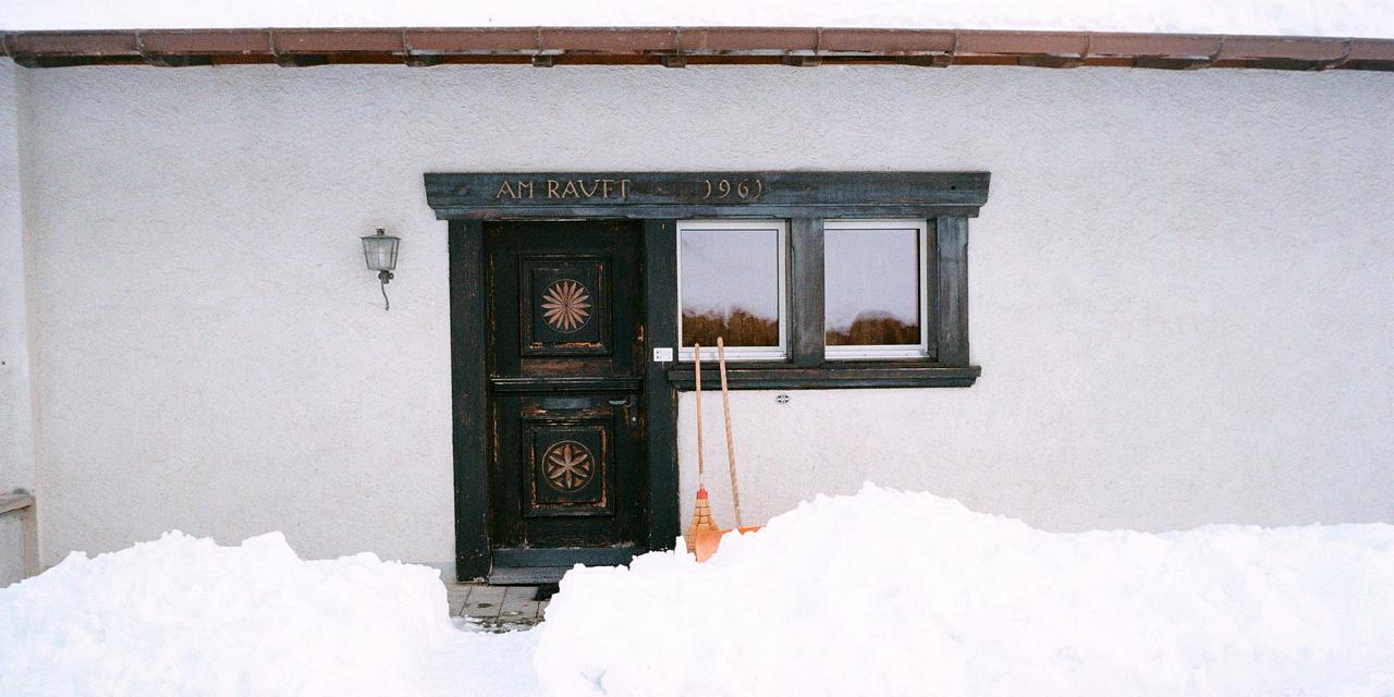 Puerta de madera tallada de una casa encalada, con la nieve a la altura de la ventana