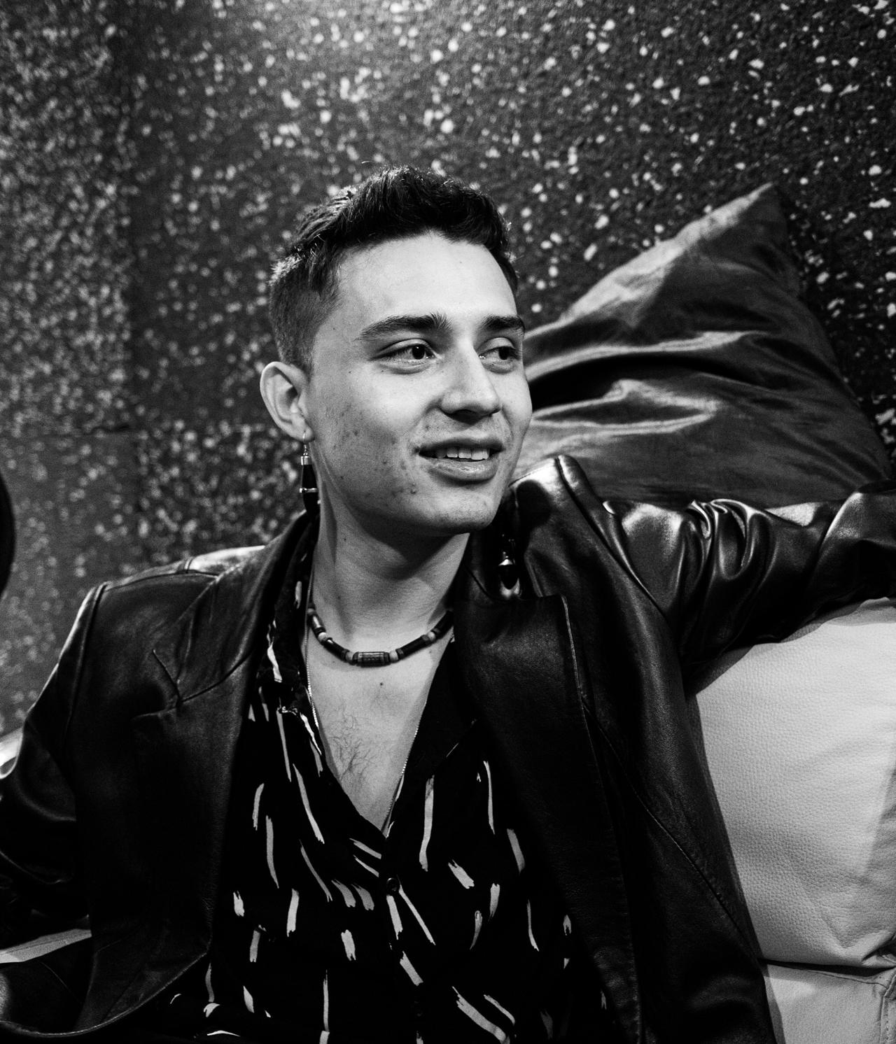 Joven sonriente con chaqueta de cuero recostado en un sofá, en blanco y negro