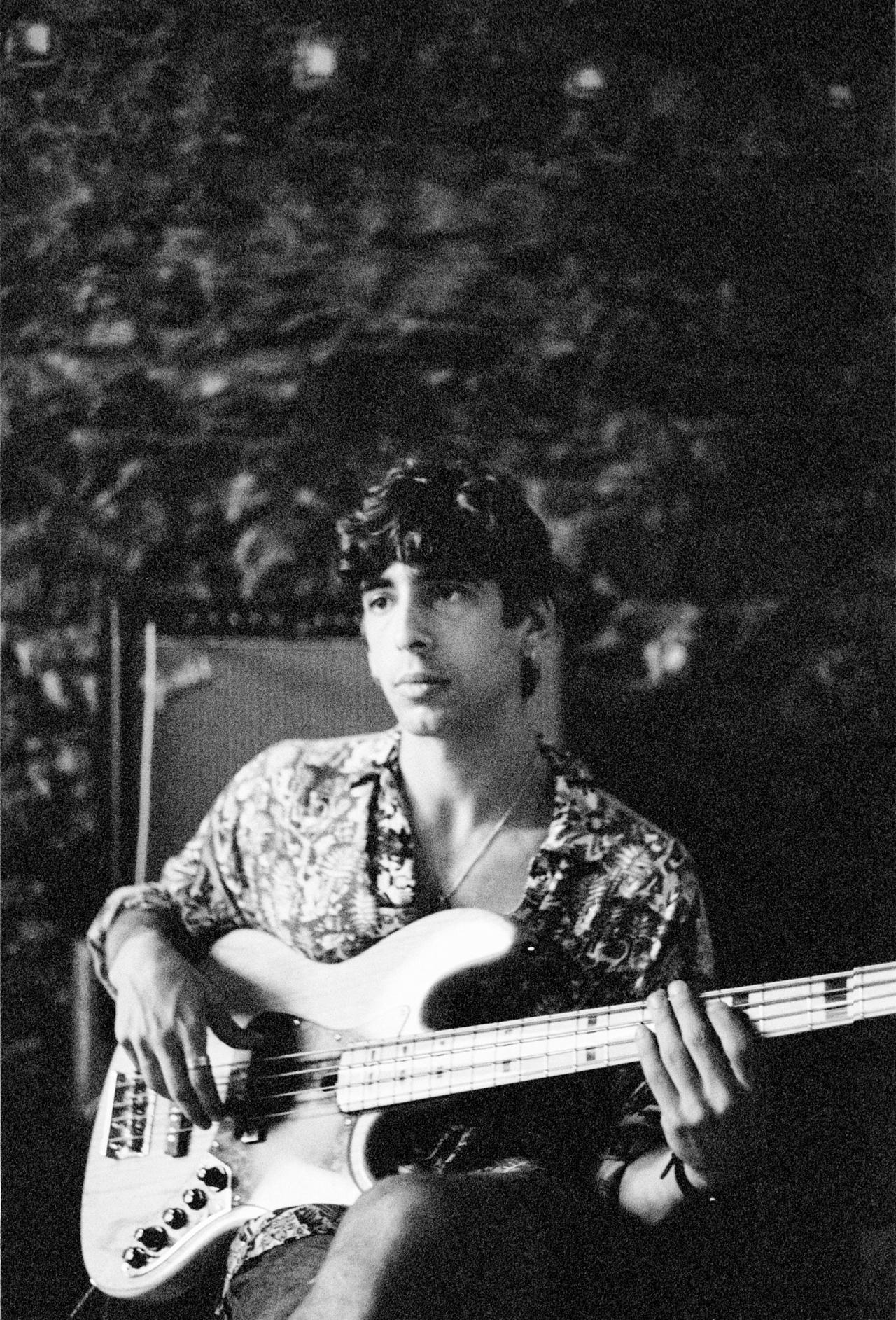 Joven con camisa estampada tocando un bajo eléctrico, en blanco y negro