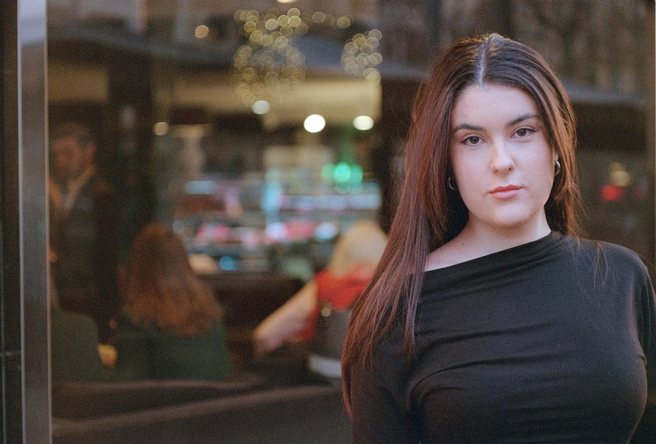 Mujer de pelo largo con jersey negro frente al escaparate de una cafetería
