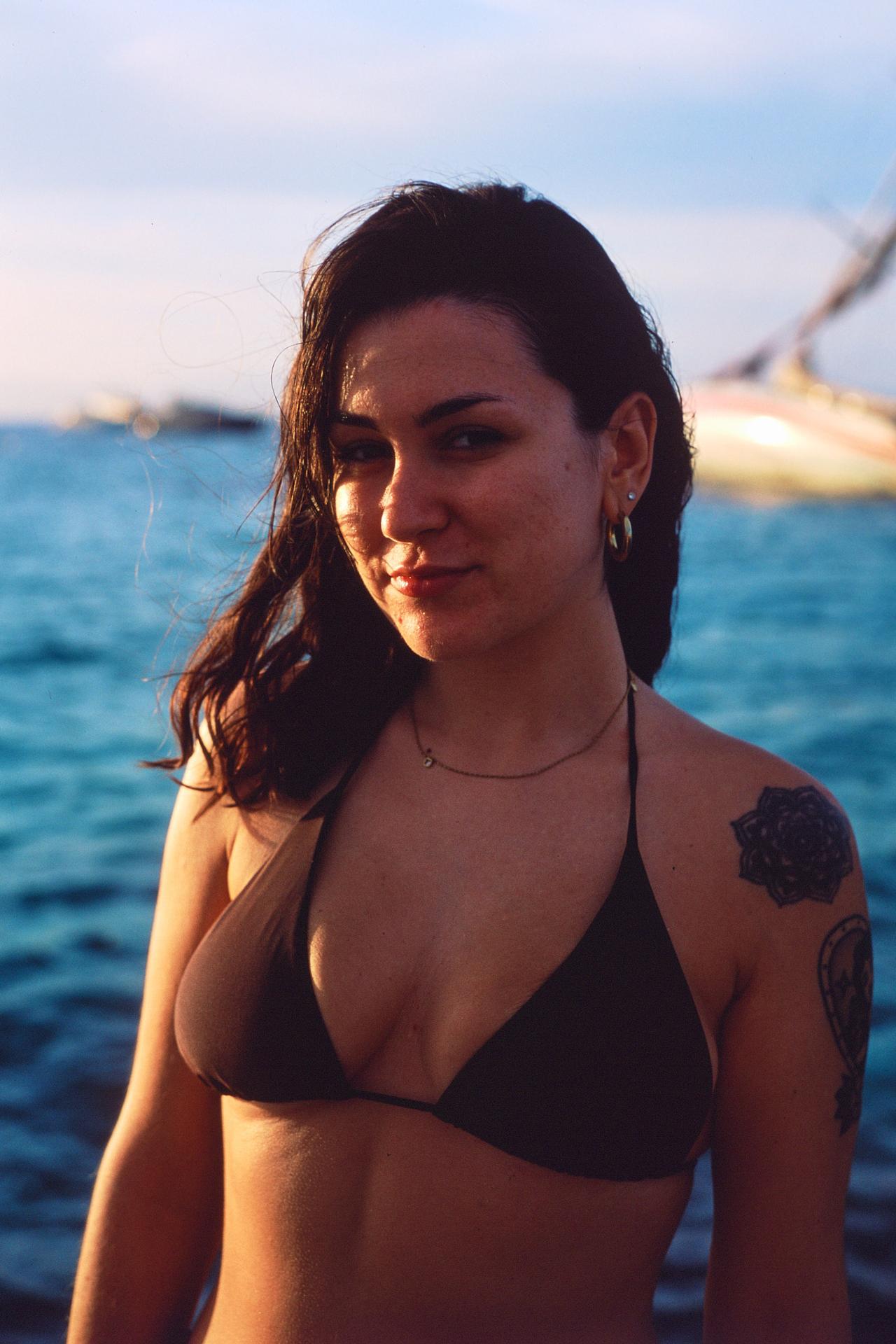 Mujer con bikini negro y el pelo mojado en el mar, con un velero al fondo