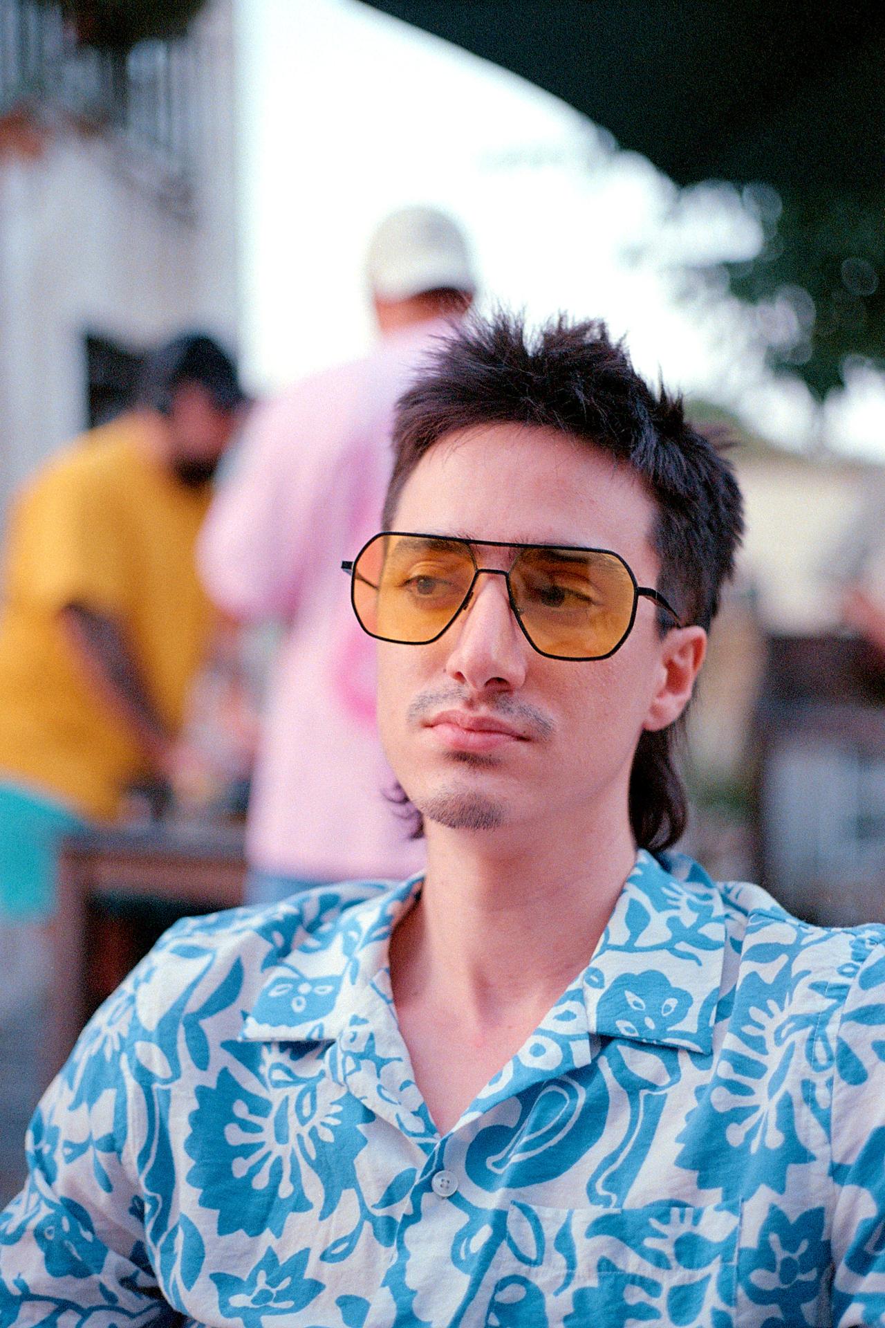 Hombre con gafas de sol tintadas y camisa estampada azul en una terraza