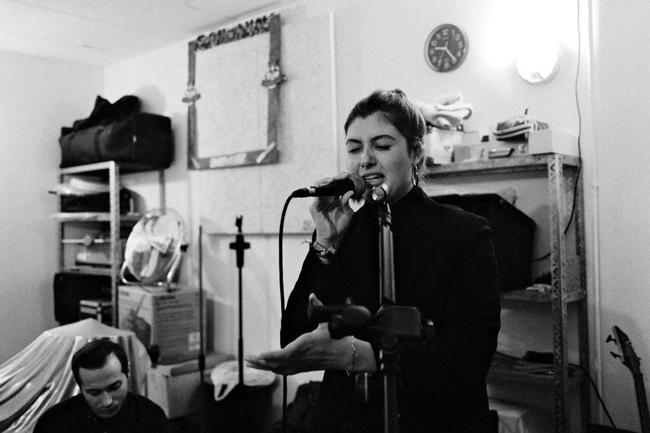 Mujer cantando ante un micrófono en un local de ensayo, en blanco y negro