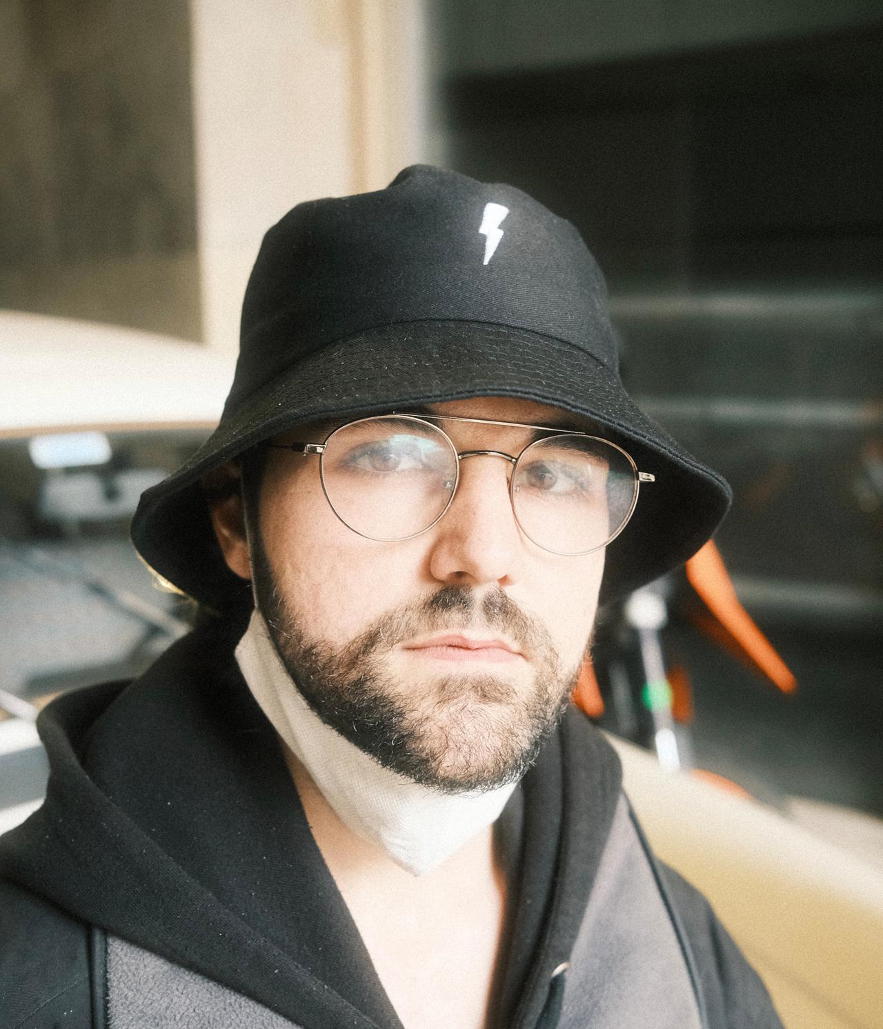 Hombre con barba, gafas redondas y gorro de pescador negro