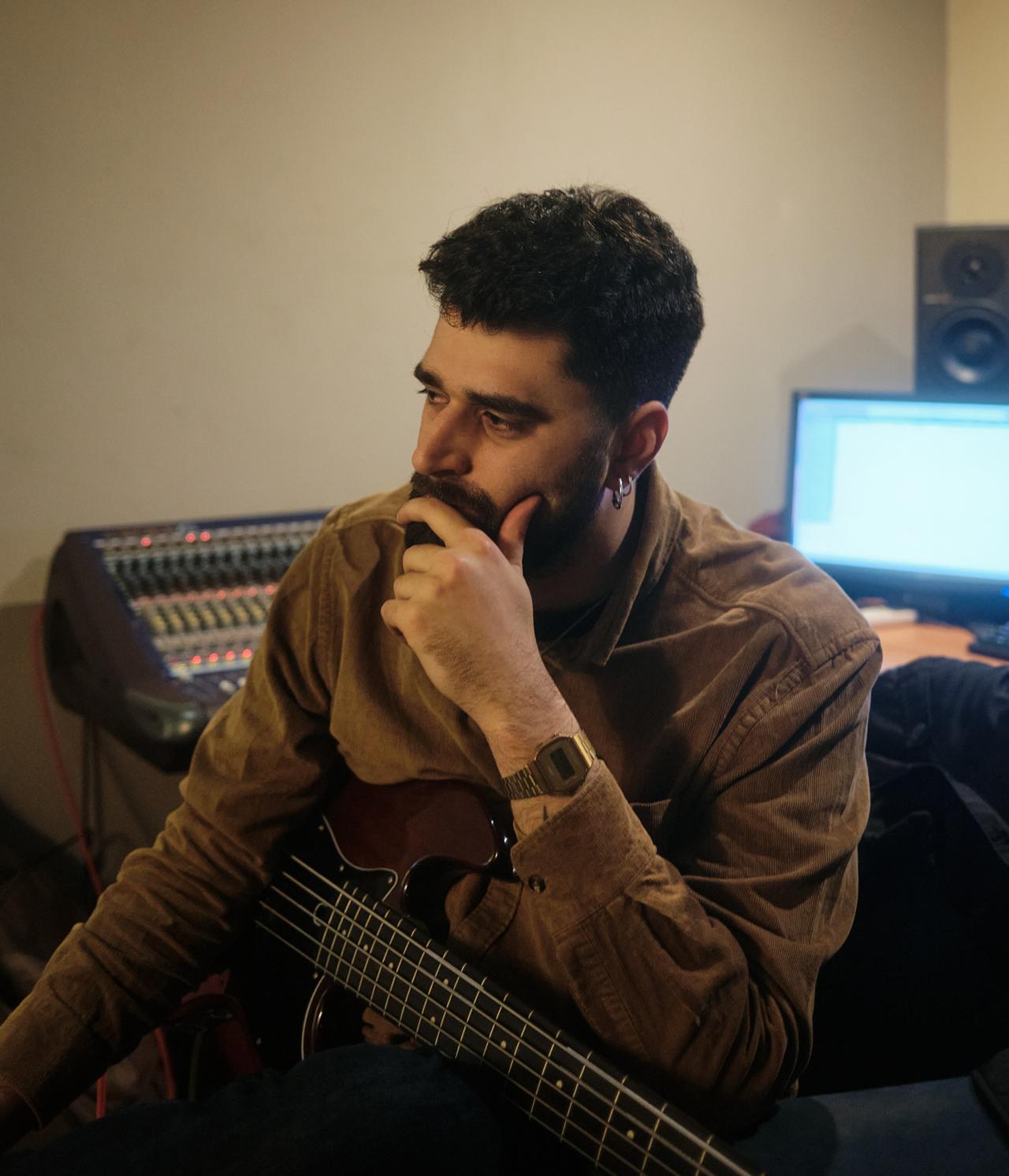 Hombre pensativo con un bajo en un estudio de grabación, junto a una mesa de mezclas