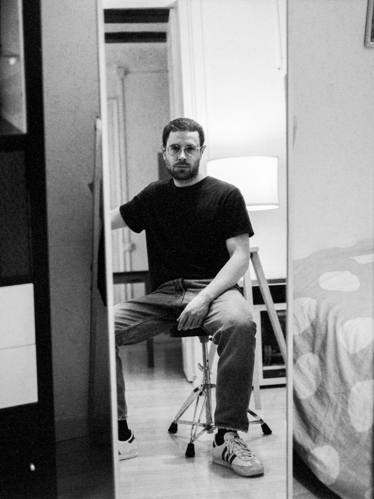 Autorretrato del fotógrafo en un espejo, sentado en un taburete, en blanco y negro