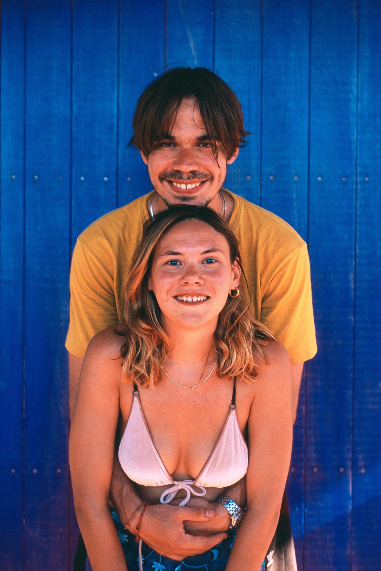 Pareja sonriente, él abrazándola por detrás, frente a una puerta de madera azul