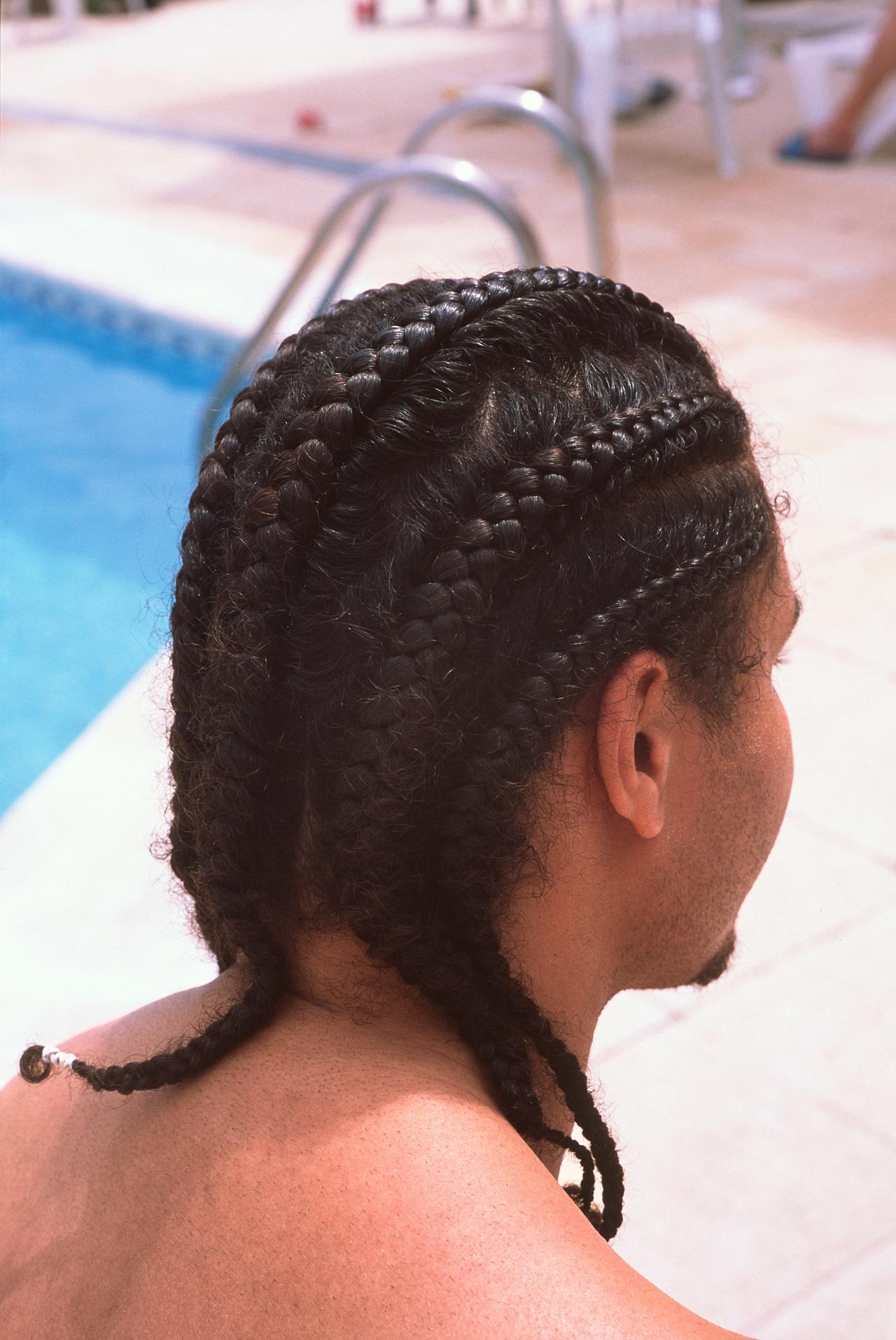 Hombre de espaldas con trenzas pegadas a la cabeza, junto a una piscina