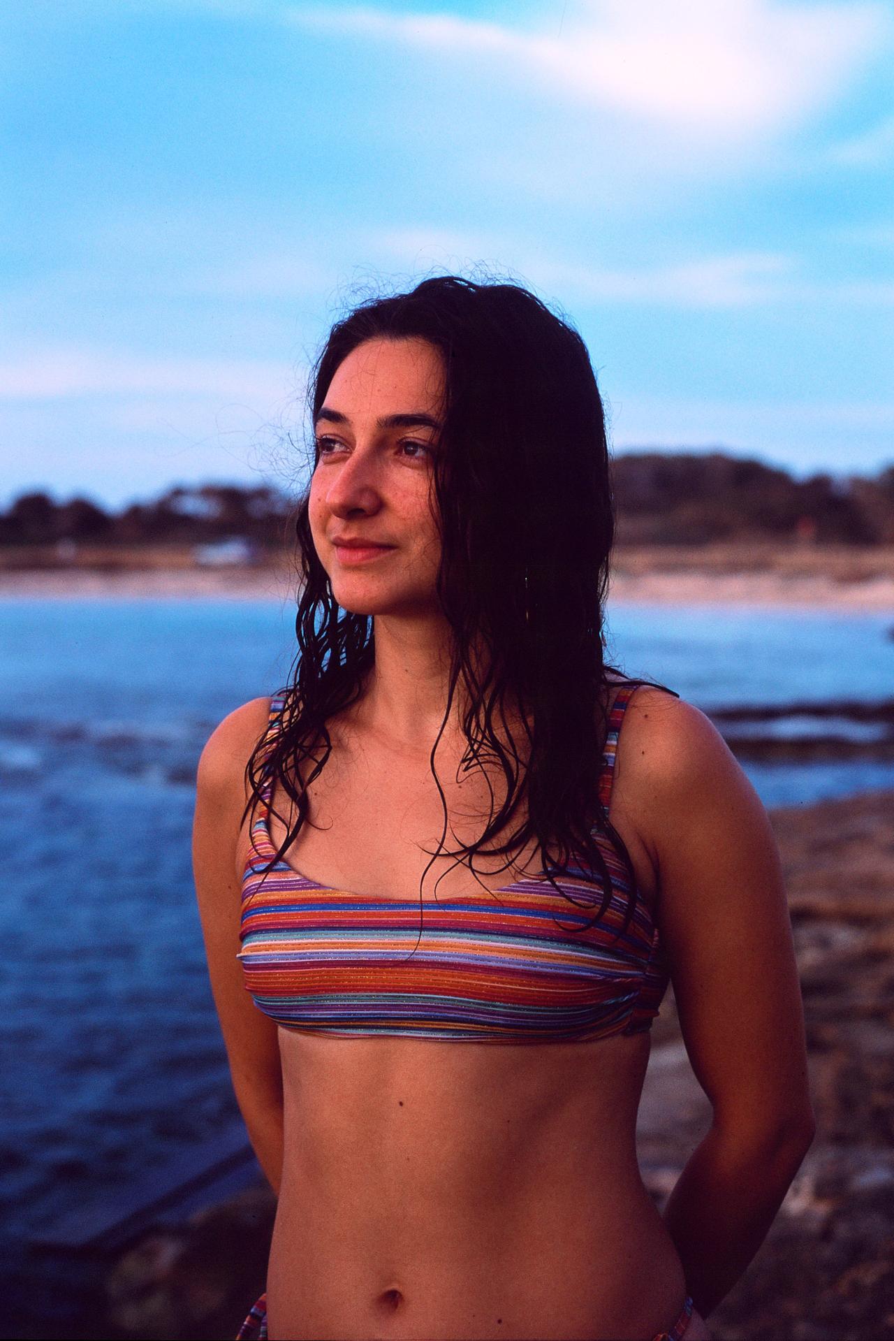Mujer con el pelo mojado y bikini de rayas junto al mar al atardecer