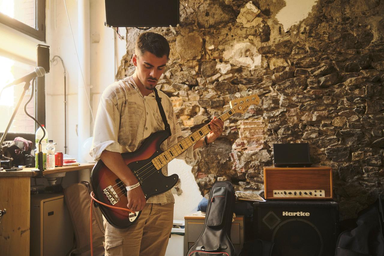 Joven tocando un bajo eléctrico en un local de ensayo con pared de piedra