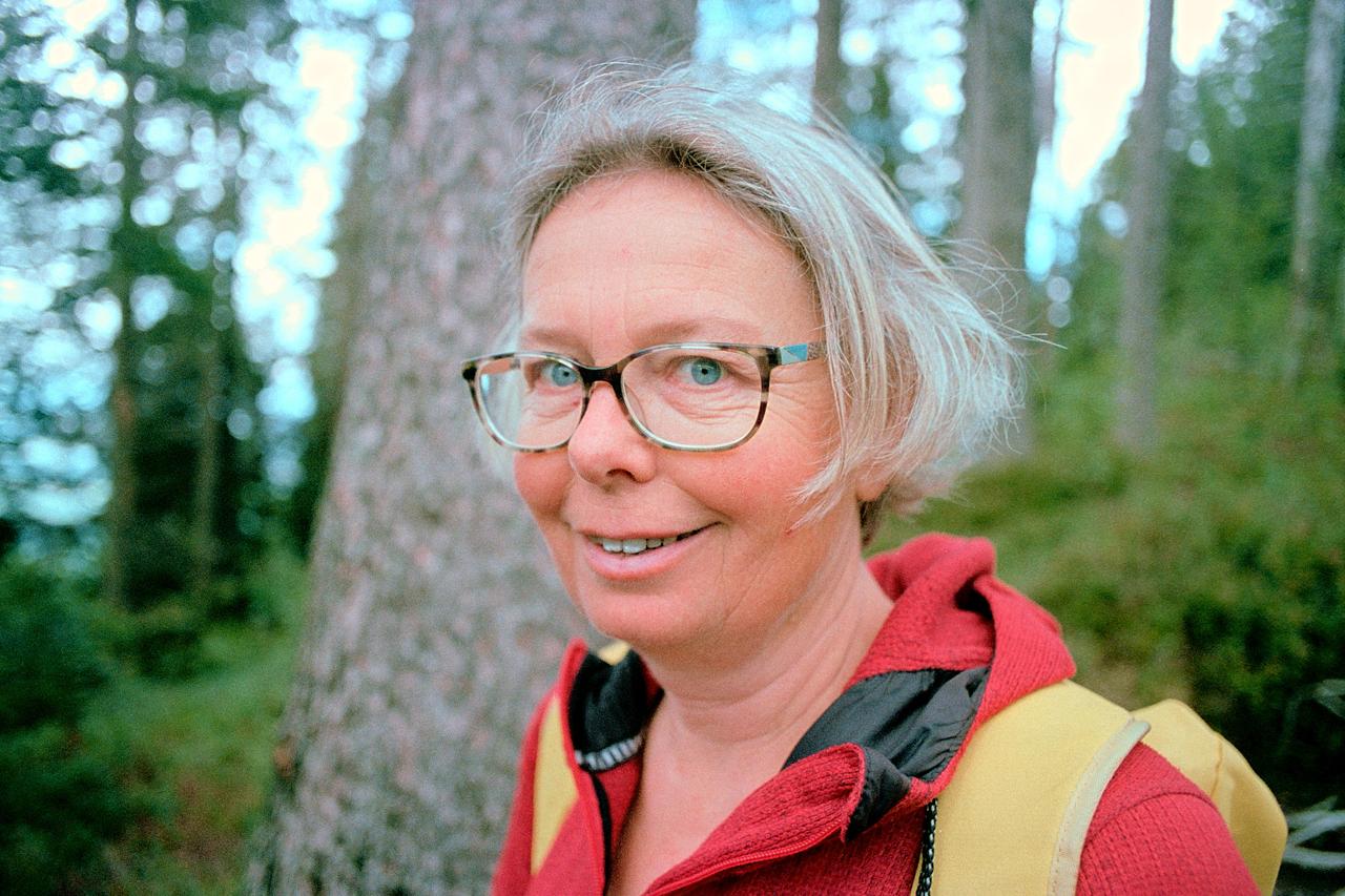 Mujer sonriente con gafas y chaqueta roja en un bosque