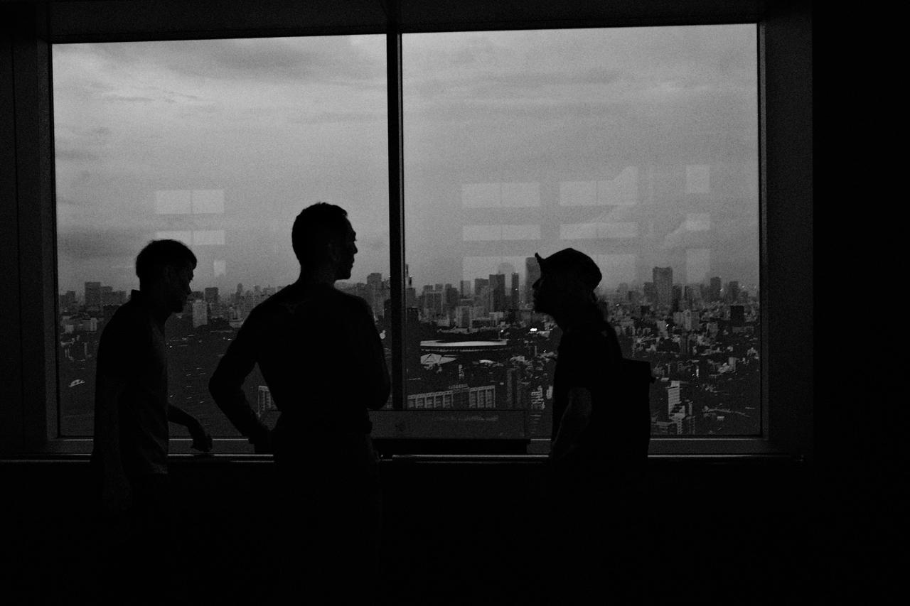 Tres personas a contraluz conversando frente a un ventanal sobre la ciudad de Tokio