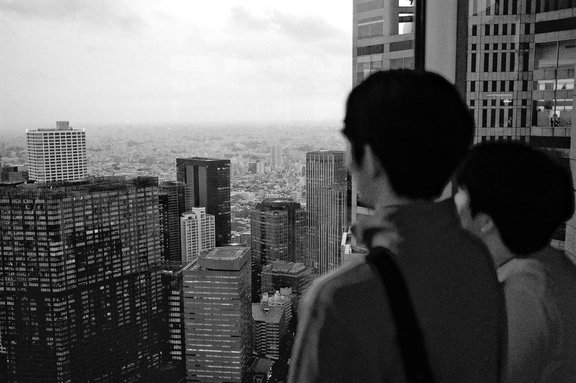 Dos personas de espaldas contemplando los rascacielos de Tokio desde un mirador en altura, en blanco y negro