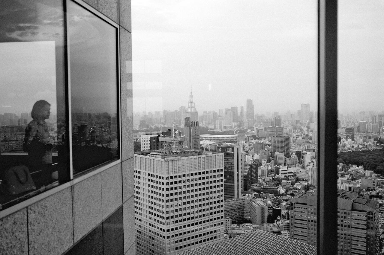 Mujer reflejada en el ventanal de un mirador, junto a una vista de rascacielos de Tokio